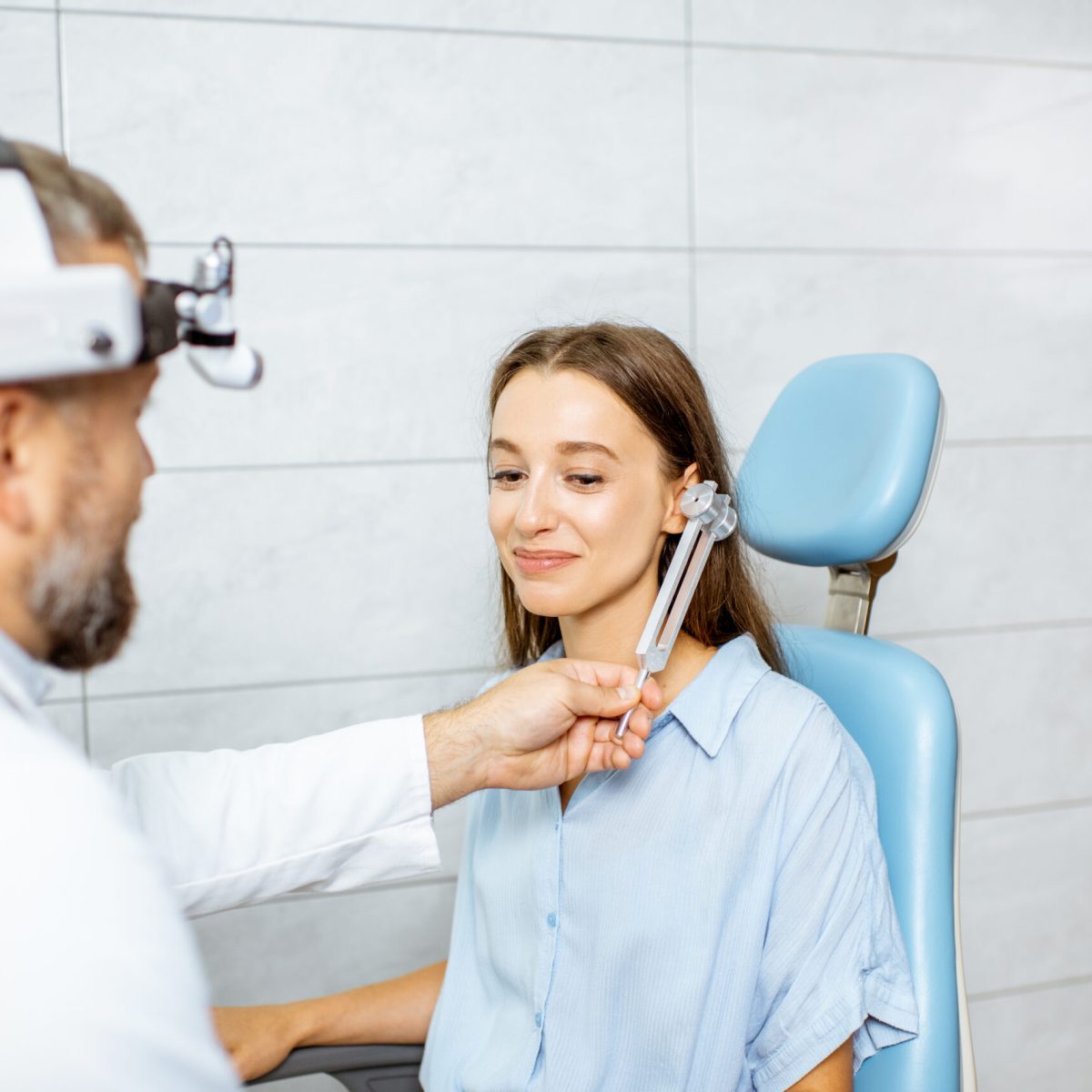 Senior otolaryngologist examining ears with ENT tuning fork for a young patient in the medical office. Hearing test with tuning fork concept