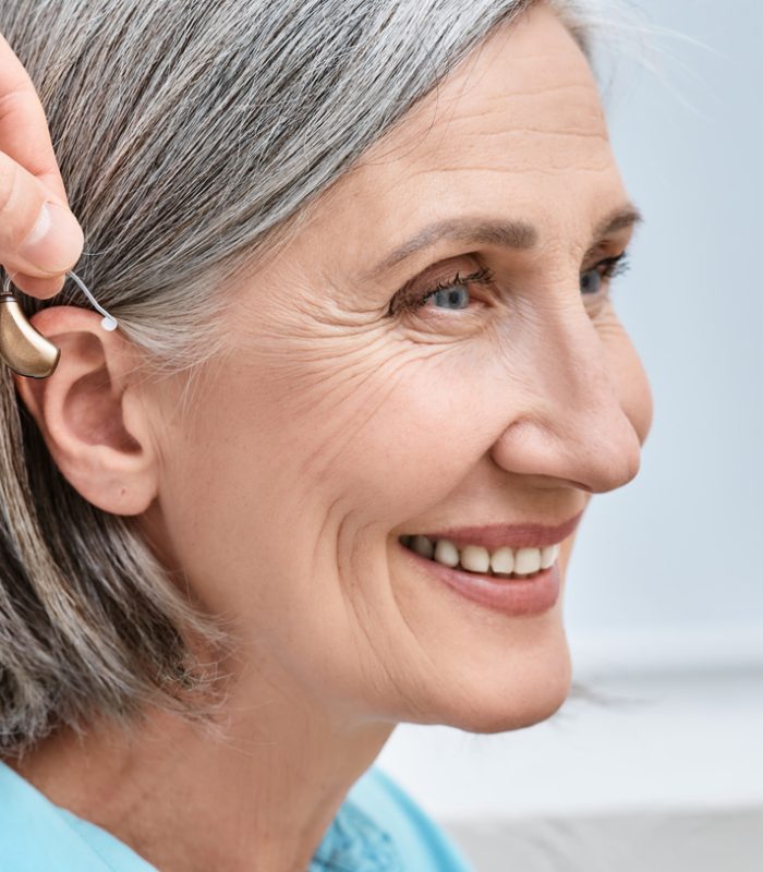 Close-up of hearing aid near senior female patient’s ear at audiology clinic. Hearing solutions, hearing BTE aids Close-up of hearing aid near senior female patient's ear at audiology clinic. Hearing solutions, hearing BTE aids